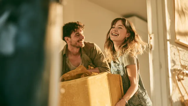 Two friends in their 20s laughing as they carry a sofa into a sunny new apartment paid for partly with a $1,500 loan
