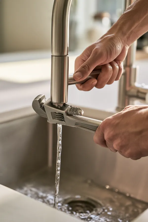 Hands tighten a new brushed-steel kitchen faucet with an adjustable wrench over a clean modern sink