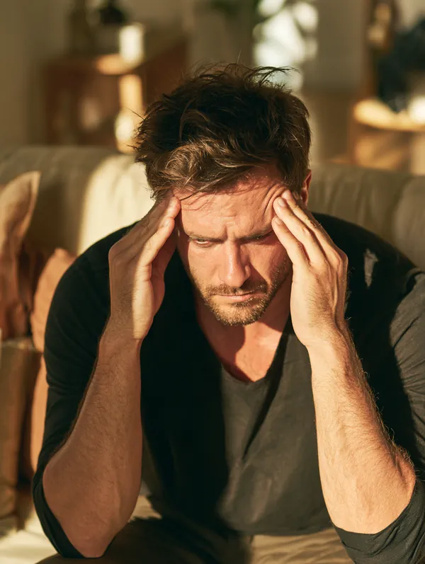 Man in his 30s rubbing his temples on his sofa with a thoughtful expression while weighing his debt options