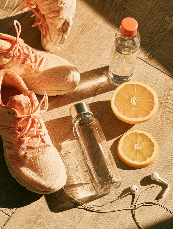 Top-down flat lay of bright running shoes, a reusable water bottle, sliced oranges and wireless earbuds on a light oak table, a fresh-start theme for Tripoint Lending debt consolidation