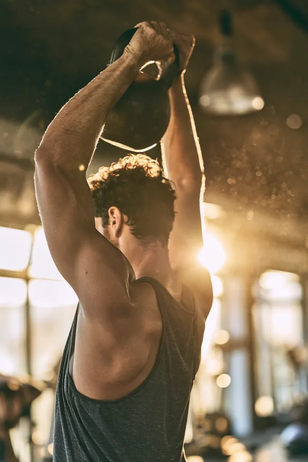 Over-the-shoulder view of a man in his 20s lifting a kettlebell in a bright gym, a reminder that a Tripoint Lending payoff plan builds strength step by step