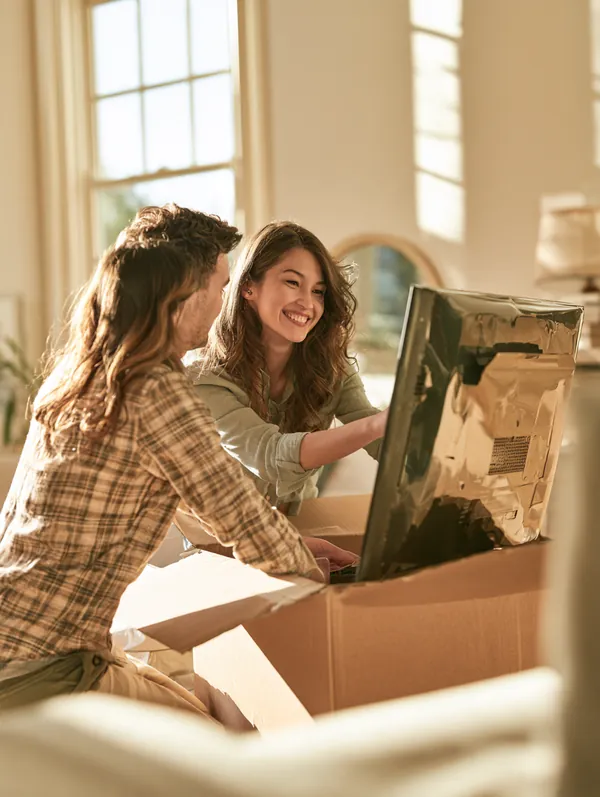 Couple in their 30s unboxing a new flat-screen TV in their living room after comparing financing options with Tripoint Lending