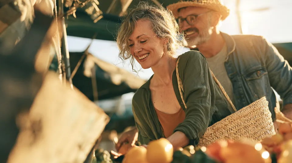 Couple in their 40s choosing fresh produce at an outdoor farmers market with a woven basket, budgeting after reviewing Tripoint Lending rates